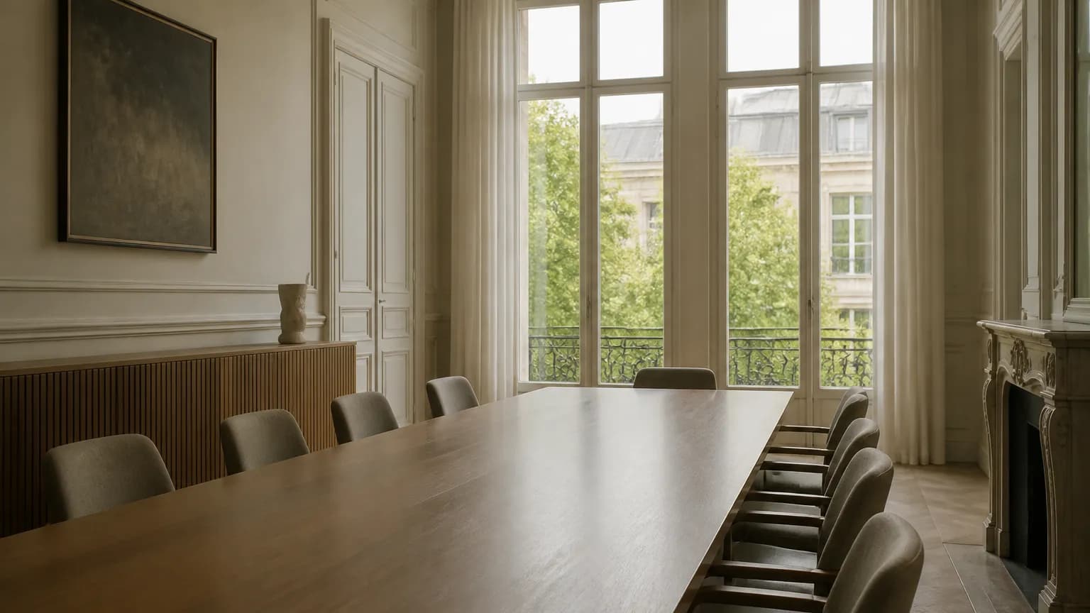 Une salle de réunion vide, longue table et chaises alignées devant une grande fenêtre donnant sur des immeubles.