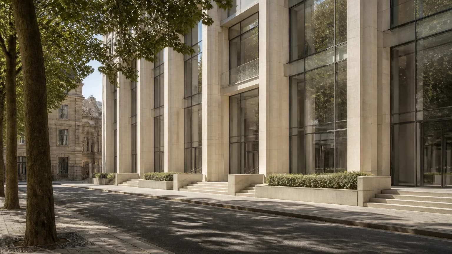 Une longue façade contemporaine à colonnes claires bordant une rue plantée d'arbres.